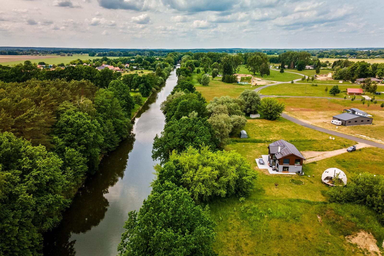 Haus am Fluss mit Garten und Wald. Blick auf ruhige Landschaft.