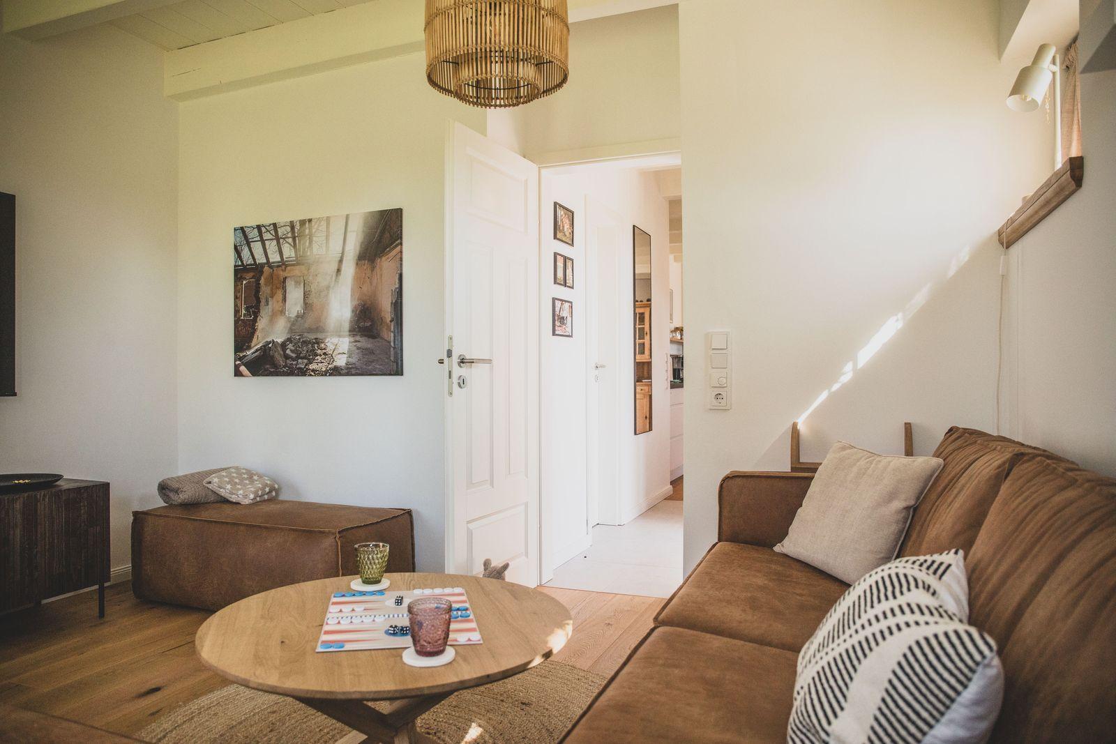 Wohnzimmer mit Sofa, runden Tisch und Wandbild. Durchgang zur Küche.