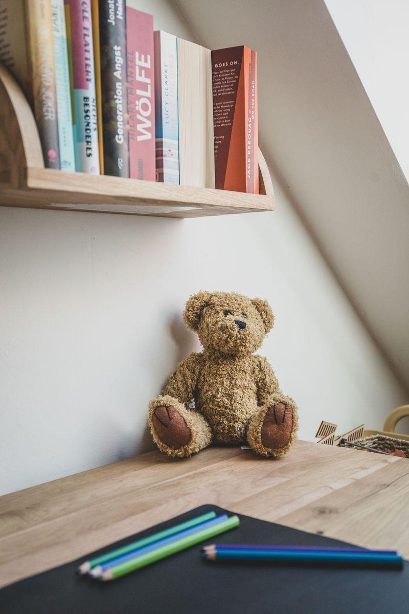 Ein Teddybär sitzt auf einem Holztisch unter einem Bücherregal.