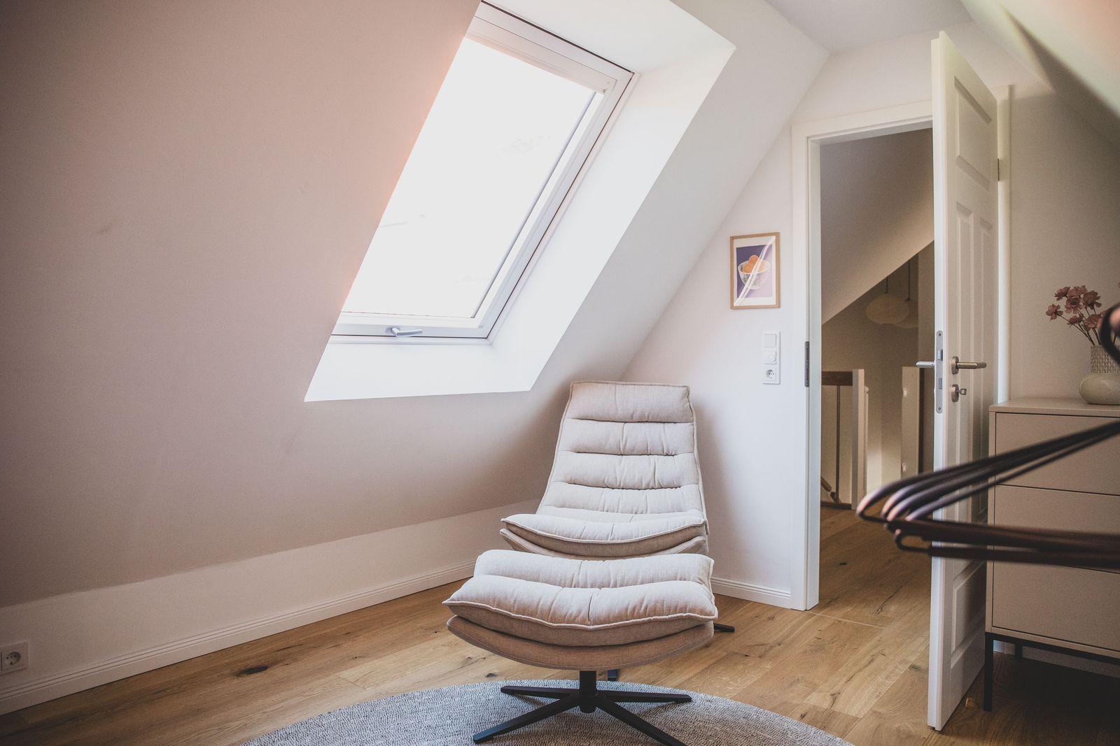 Dachgeschosszimmer mit Sitzgelegenheit und Dachfenster. Holzboden und offene Tür.