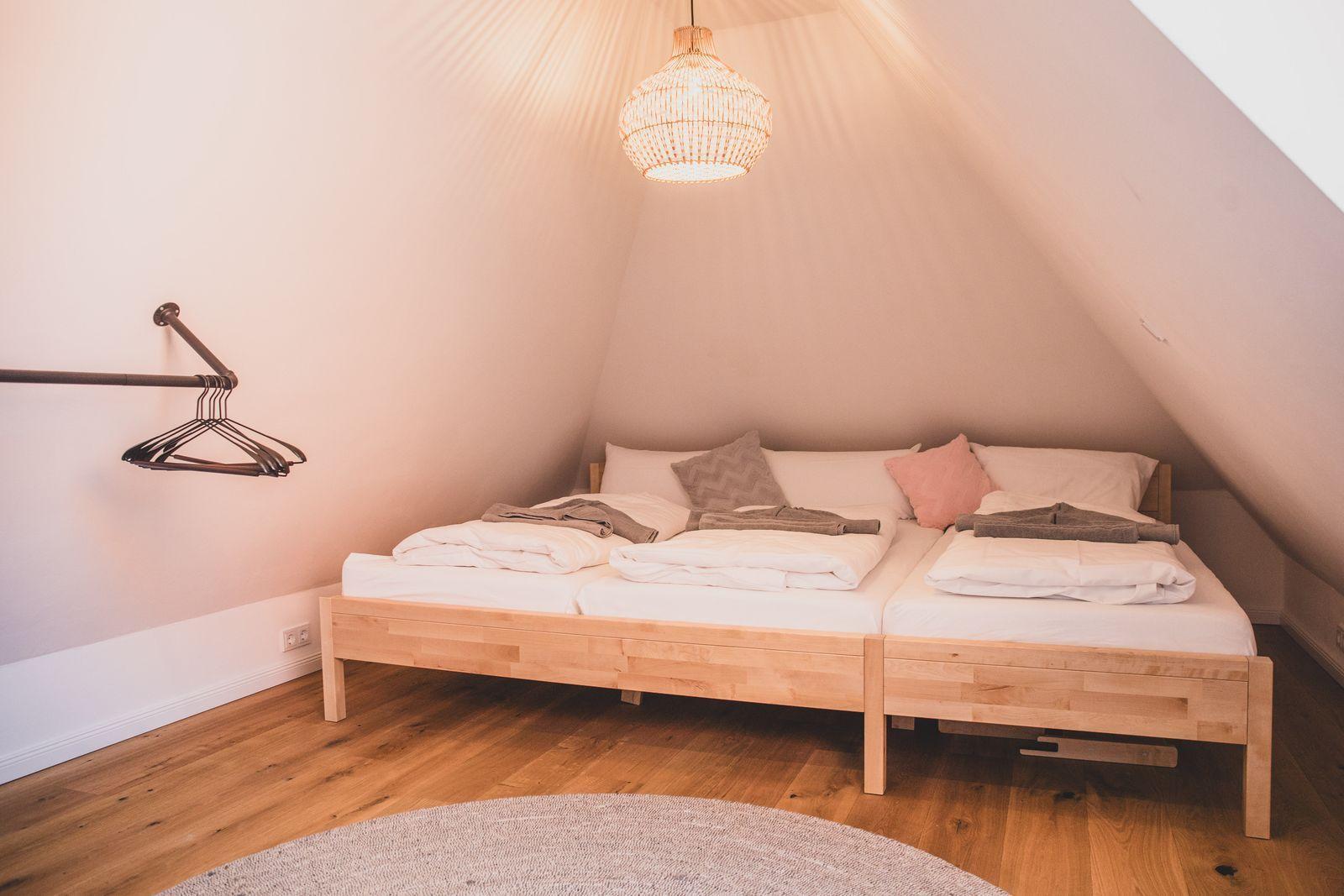 Schlafzimmer mit Doppelbett, Holzboden und Wandleuchte unter schrägen Dachdecken.