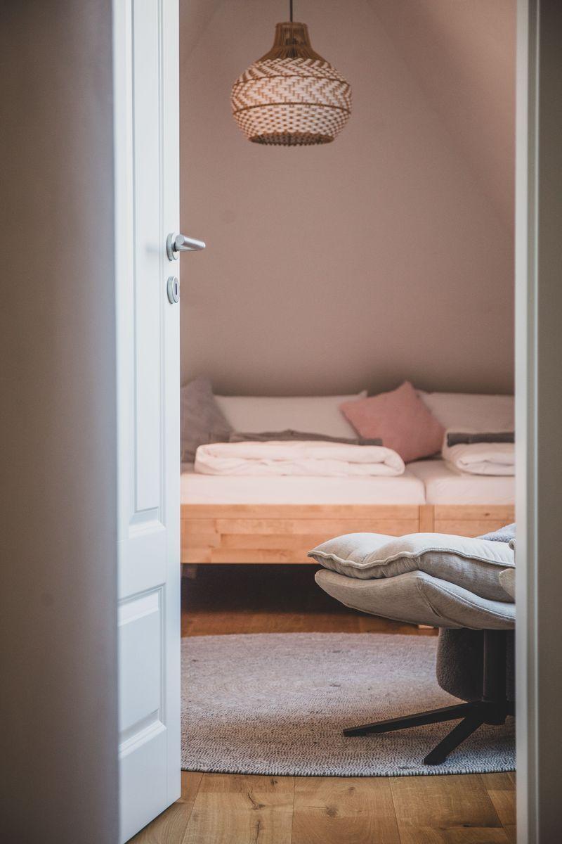 Schlafzimmer mit Bett, Decke und Sitzgelegenheit. Hängelampe und Holzboden.
