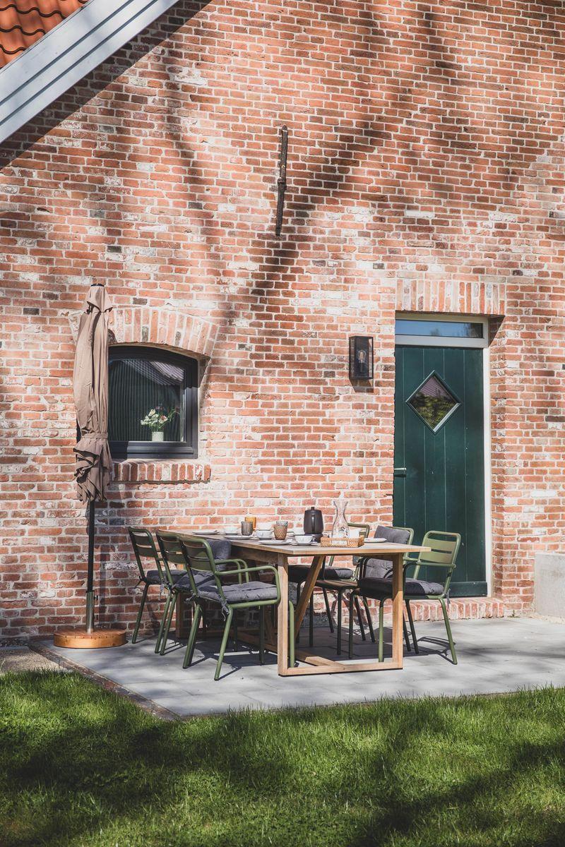 Außenbereich mit Tisch und Stühlen vor Backsteinhaus mit grüner Tür und Fenster