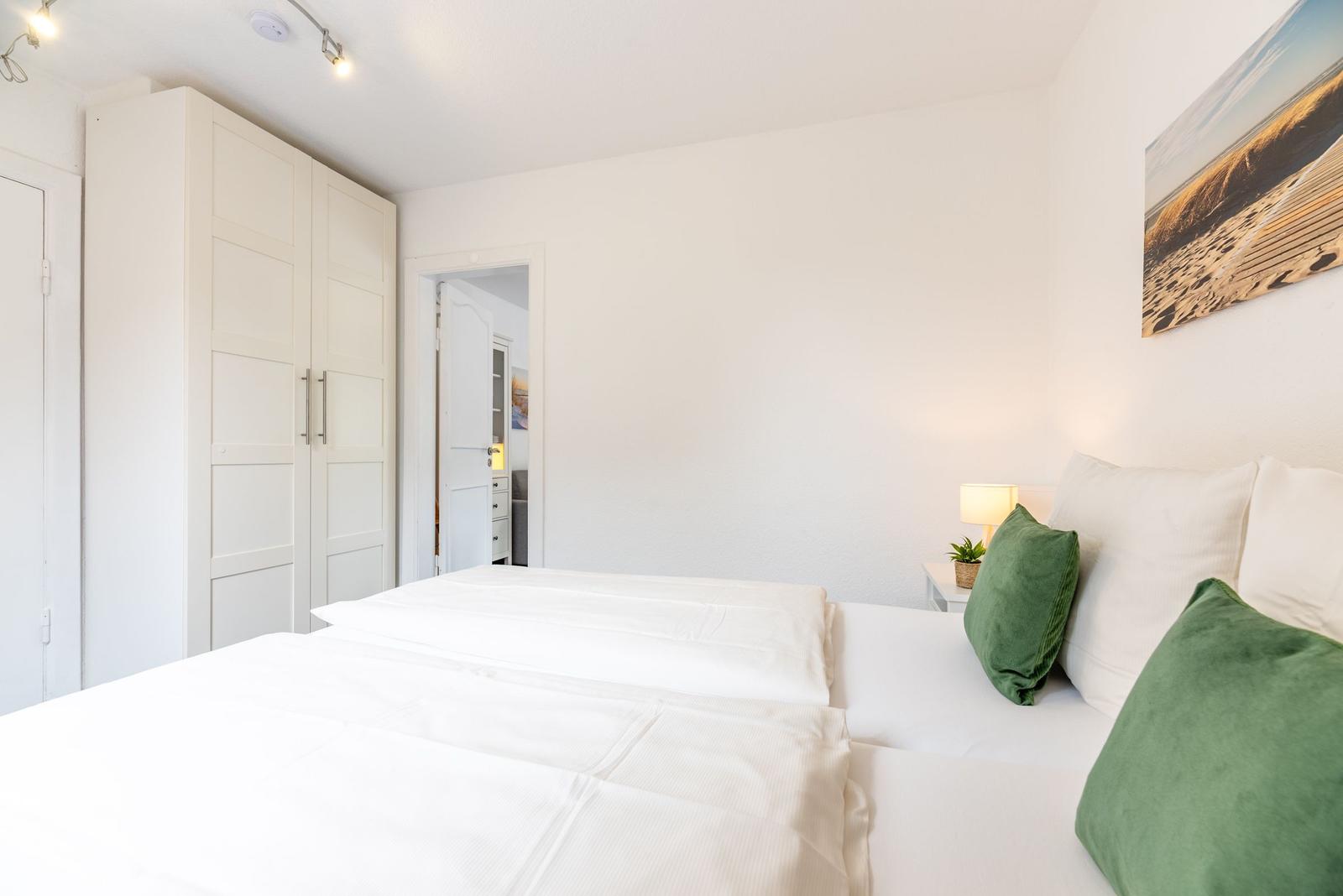 Schlafzimmer mit Doppelbett, weißen Wänden, grünen Kissen und Kleiderschrank.