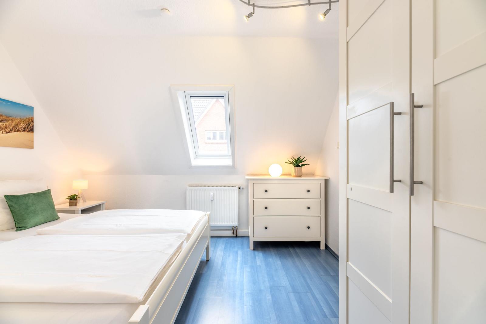 Schlafzimmer mit Dachschrägen, Bett, Schrank und kleinem Fenster
