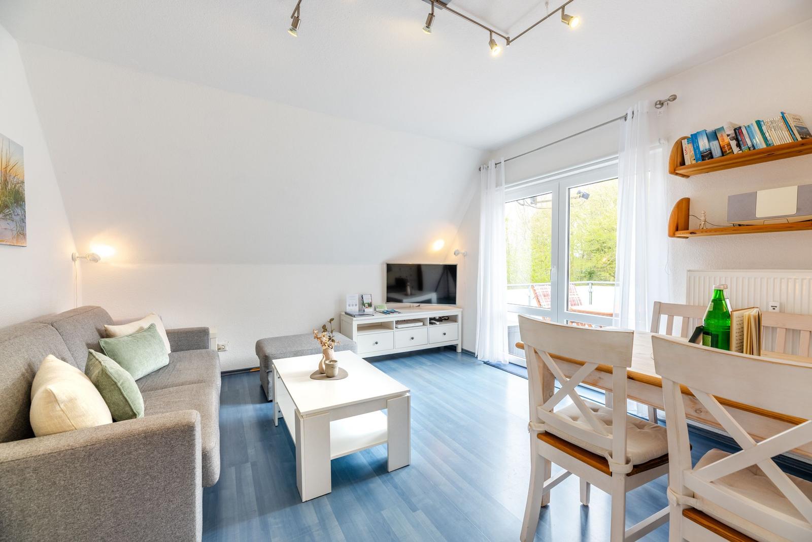 Wohn- und Essbereich mit Sofa, Tisch und TV. Fenster mit Blick auf Balkon.