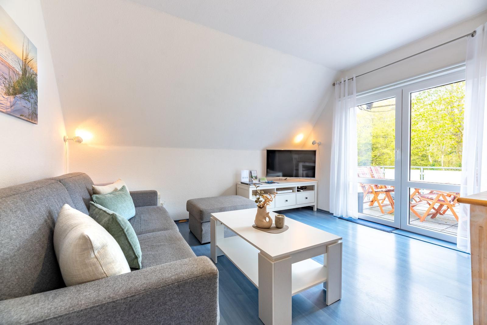Wohnzimmer mit Sofa, Couchtisch und TV. Durchgang zur Terrasse mit Gartenblick.