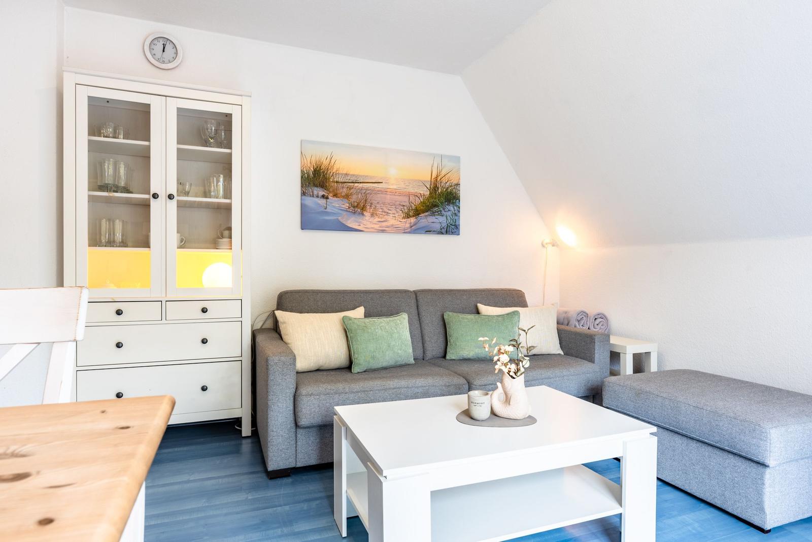 Wohnzimmer mit grauem Sofa, weißem Tisch und Bild an der Wand.