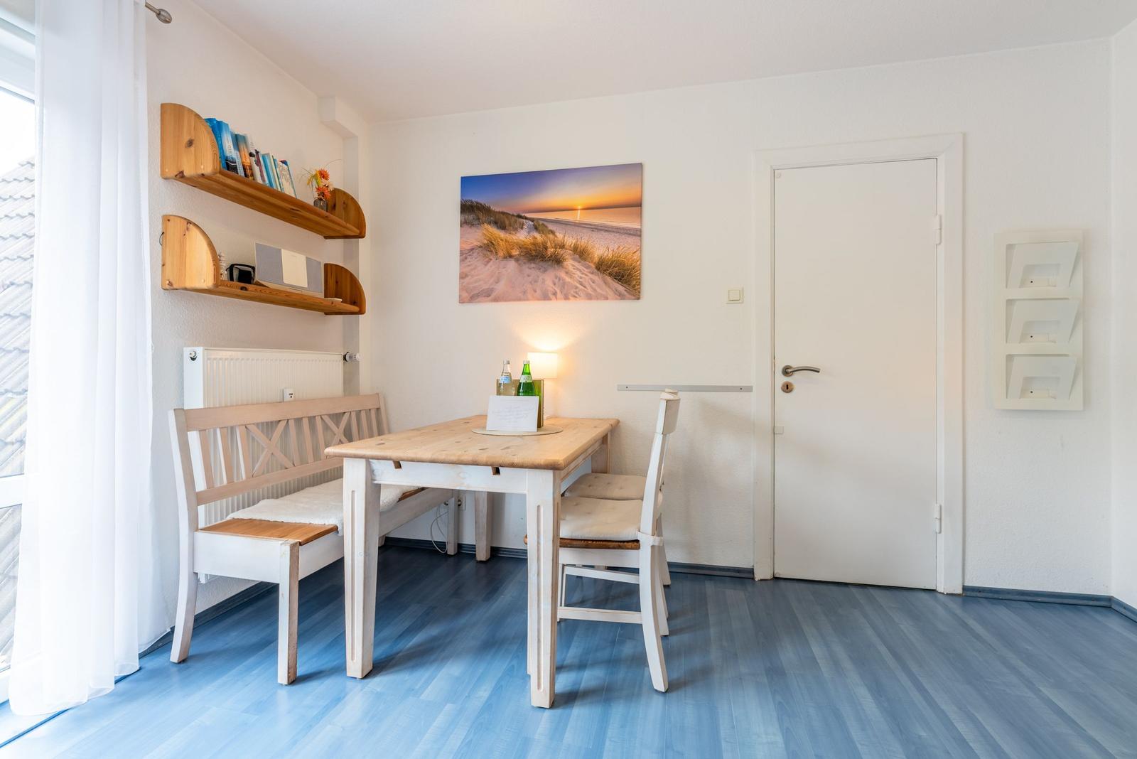 Esszimmer mit Tisch, Bank und Stühlen. Wandbild zeigt Strand bei Sonnenuntergang.