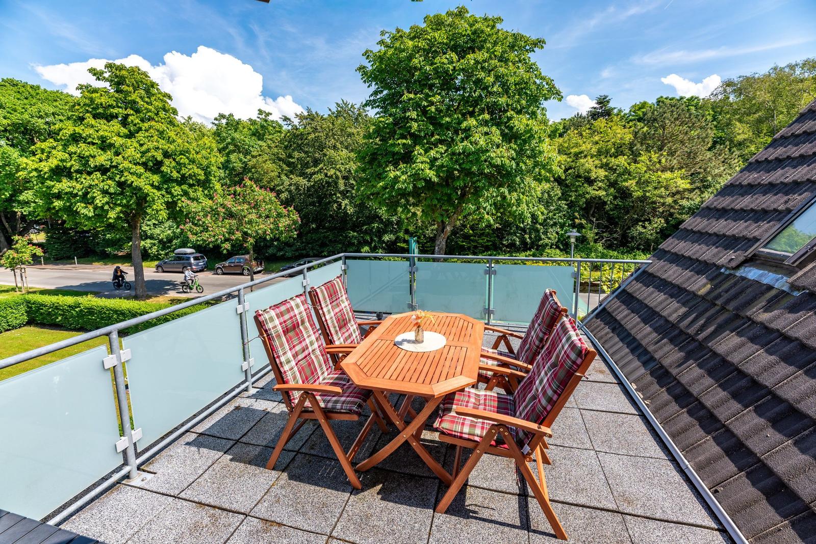 Terrasse mit Holztisch und vier Stühlen, umgeben von Grün und einem Dach.