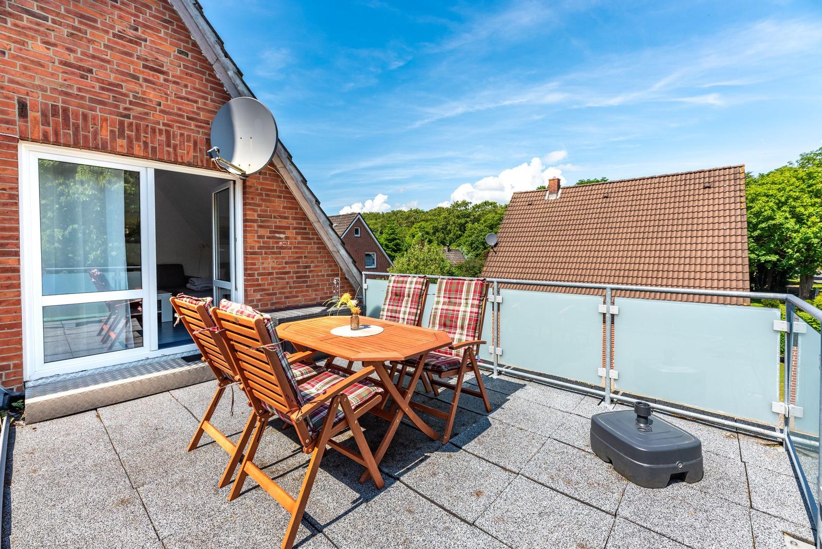 Terrasse mit Holztisch und Stühlen, Sicht auf Dächer und Bäume, Satellitenschüssel an der Hauswand.