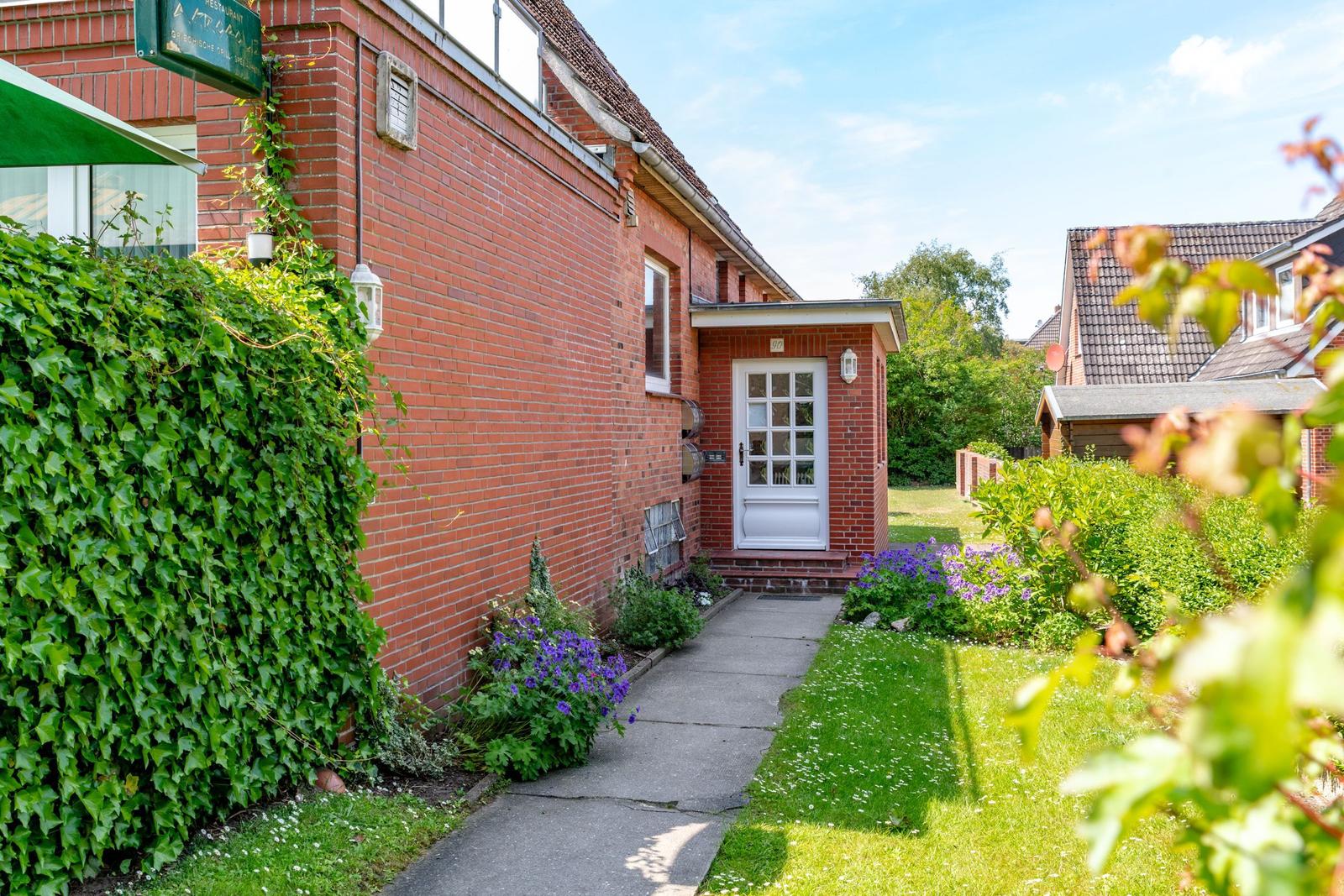 Rotes Backsteingebäude mit weißen Türen und gepflegtem Garten mit Blumen und Beete.