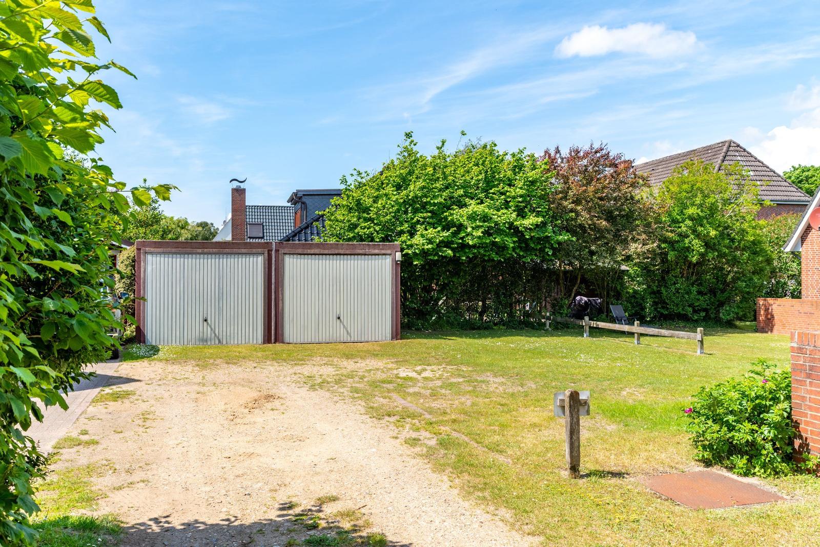 Hinterhof mit Garage, Grasfläche und Bäumen unter blauem Himmel.