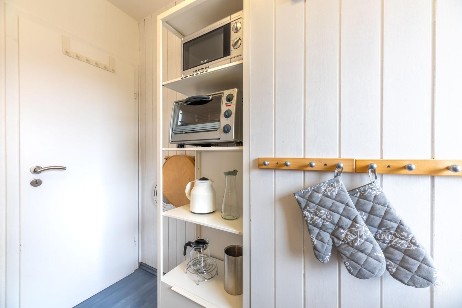 Küchenbereich mit Mikrowelle, Toaster und Kochutensilien an einem Schrank.