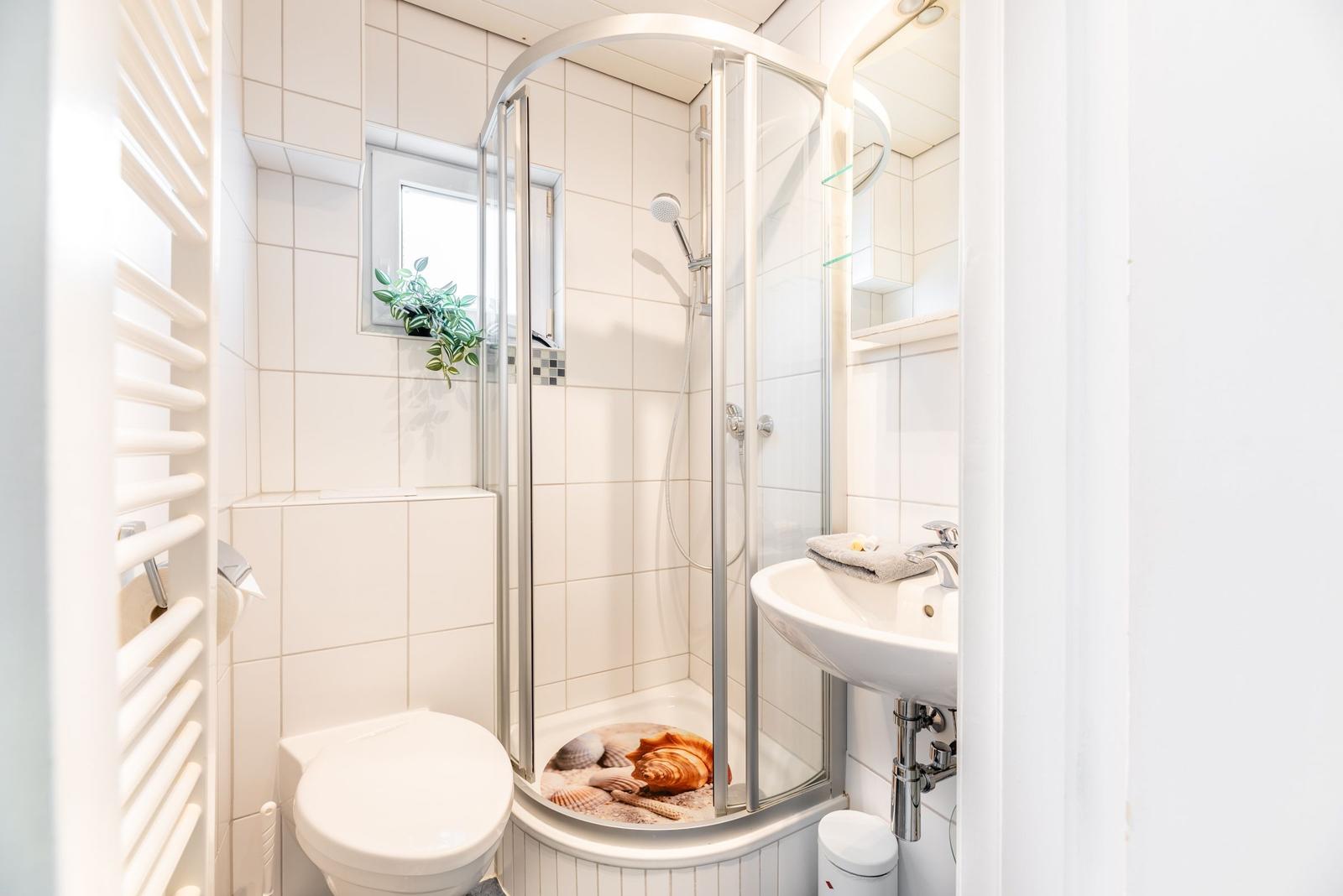 Badezimmer mit Dusche, Waschbecken und Toilette. Duschwanne mit Muschelbild.