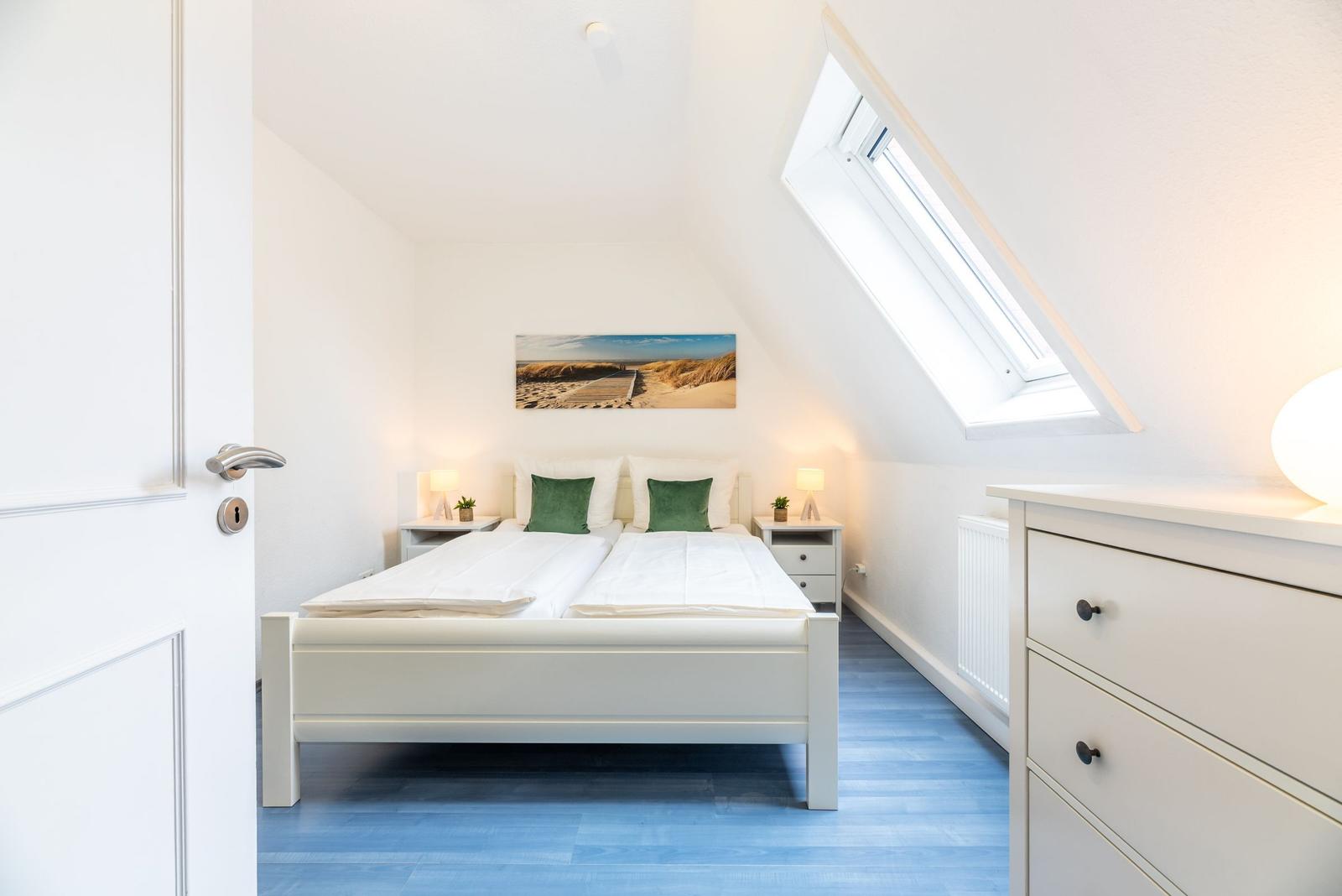 Schlafzimmer mit Dachschrägen, Doppelbett, zwei Nachttischen und Fenster.