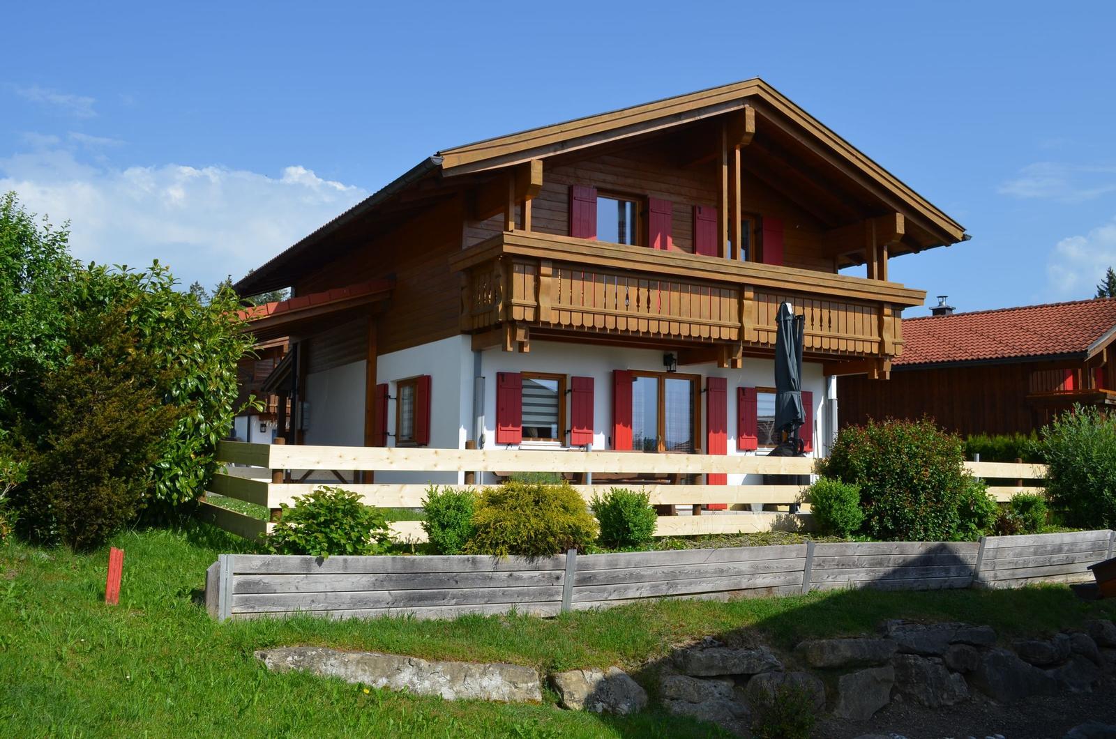 Holzhaus mit Balkon, roten Fensterläden und Gartenzaun.