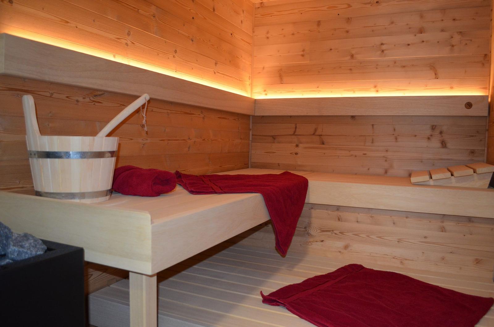 Sauna mit Holzwand, Liegeflächen und roten Handtüchern sowie einem Holzeimer.