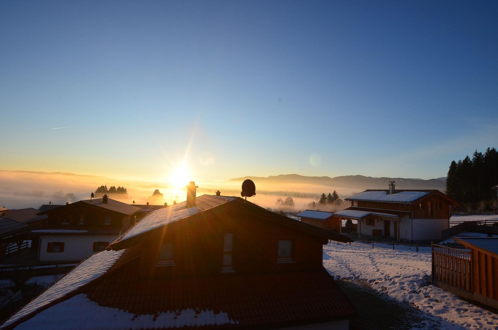 Schneebedeckte Häuser mit Sonnenaufgang über den Bergen.