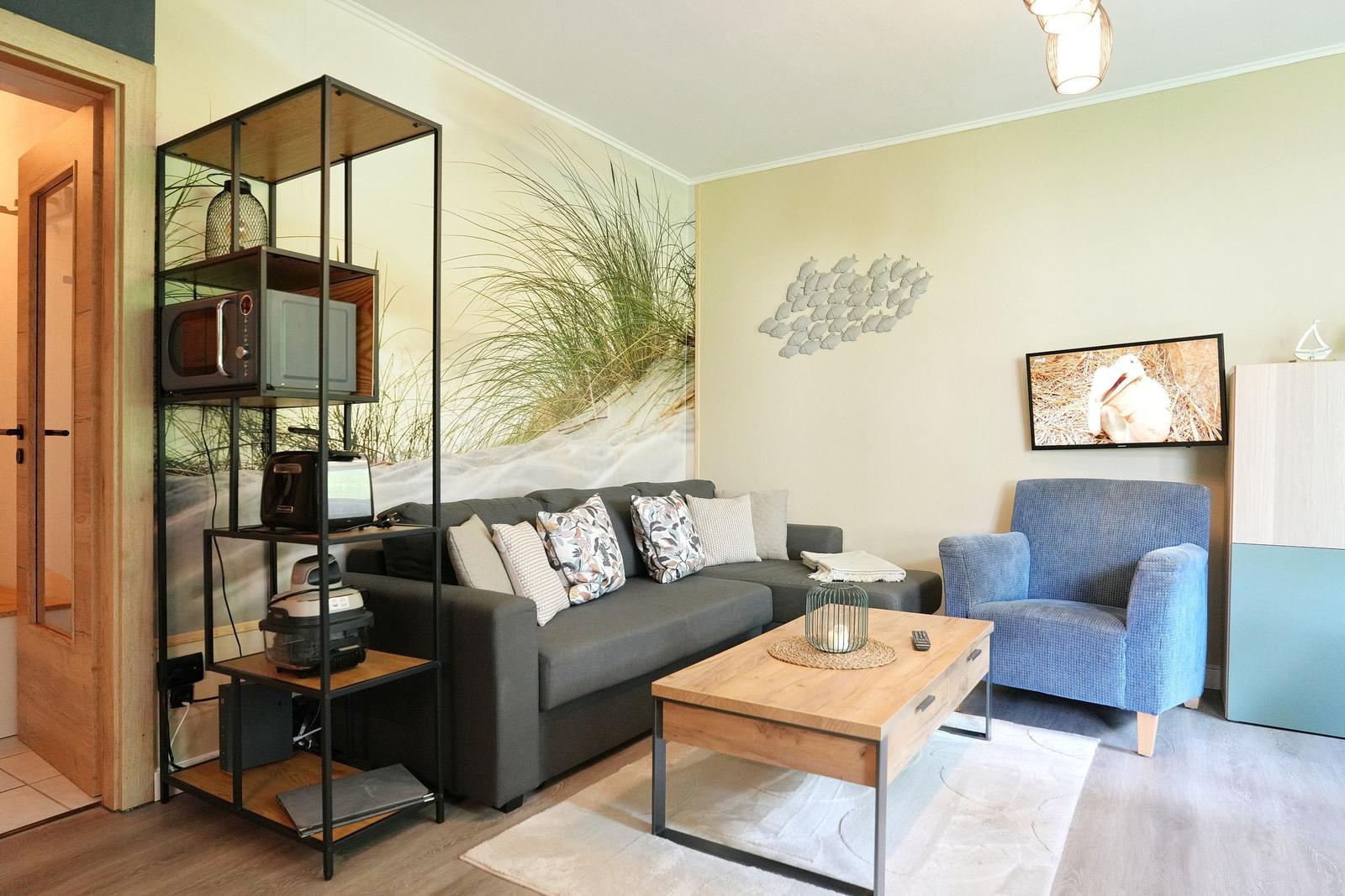 Wohnzimmer mit Sofa, Sessel, Couchtisch und Küchenzeile im Hintergrund.