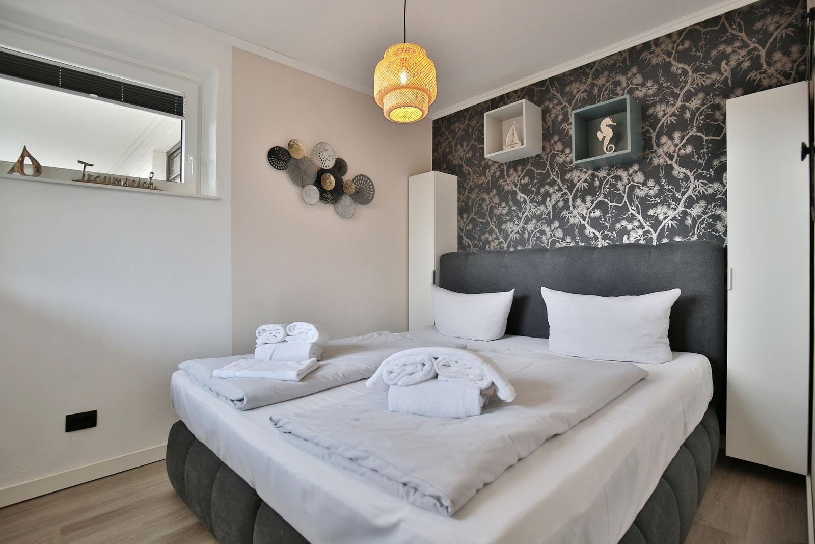 Schlafzimmer mit Doppelbett, gemustertem Wandbezug und dekorativen Wandelementen.