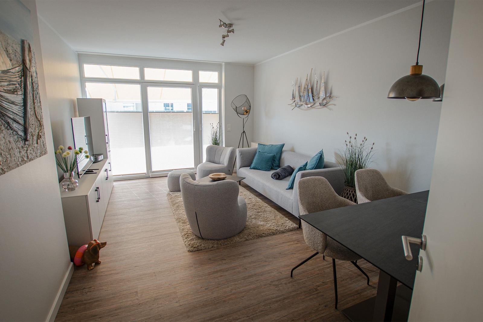 Wohn- und Essbereich mit Sofa, Sesseln und Tisch. Durchgangstür und Wanddekoration sichtbar.