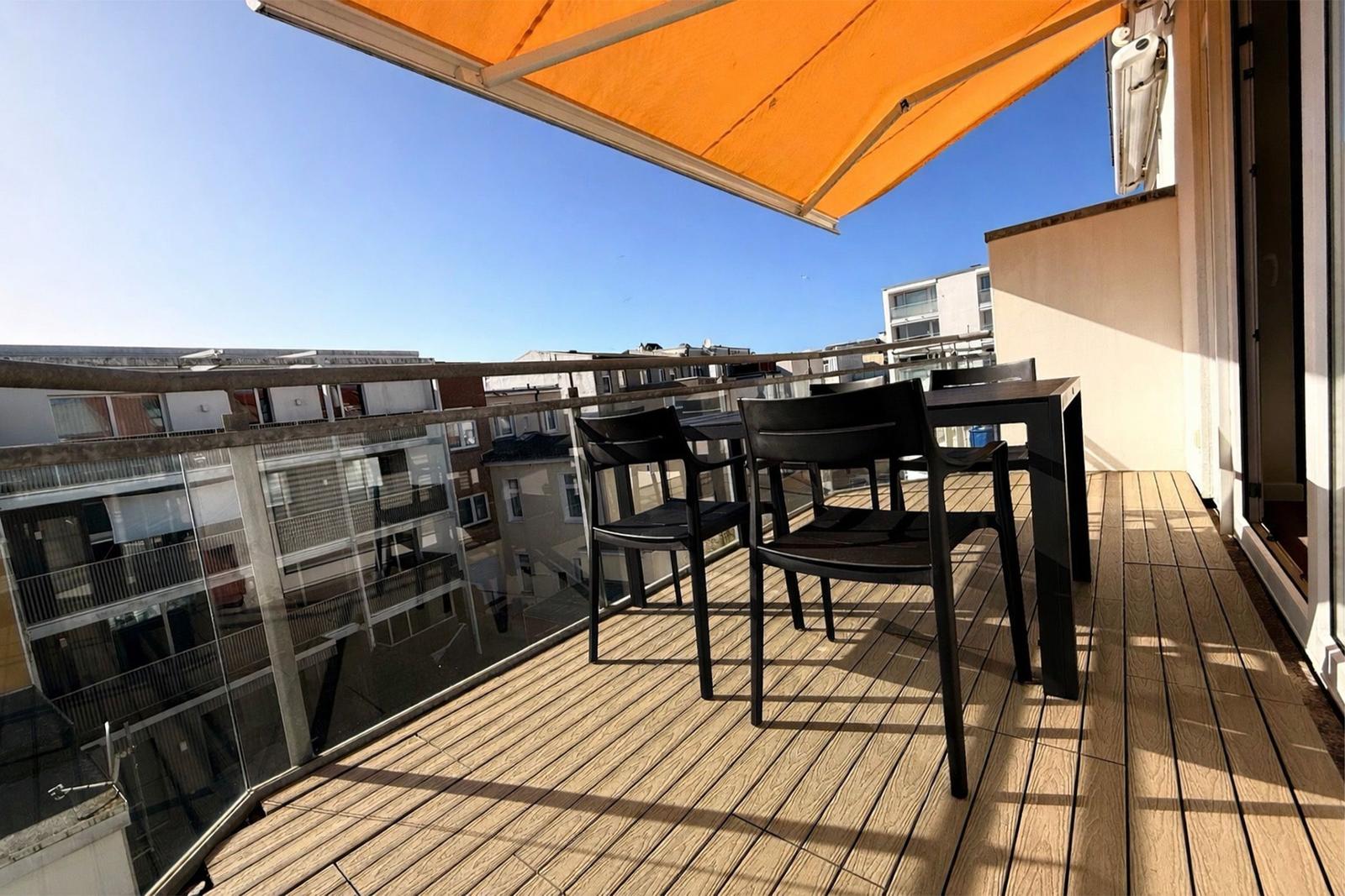 Terrasse mit Tisch, Stühlen und orangefarbenem Markisenüberdachung. Holzdeckenboden und Glasgeländer.