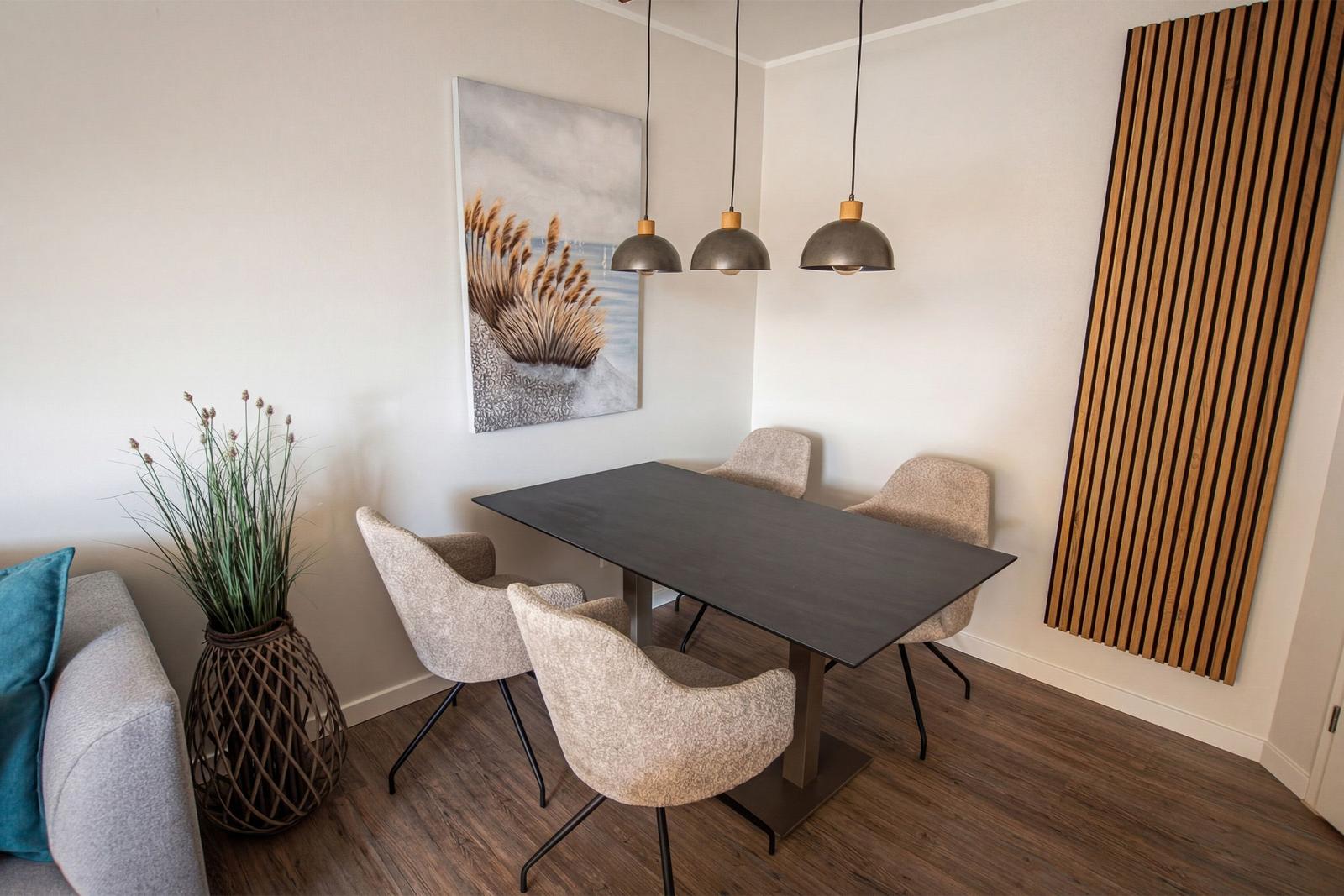 Essbereich mit Tisch, vier Stühlen und Hängelampen. Wandbild und Holzpaneel sichtbar.