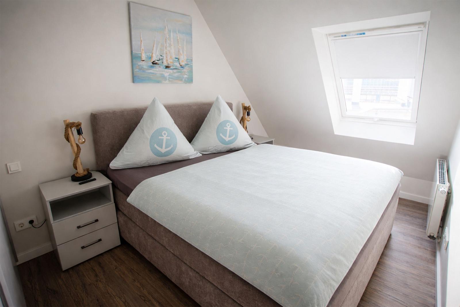Schlafzimmer mit Doppelbett, Fenster und Wandbild mit Segelbooten.