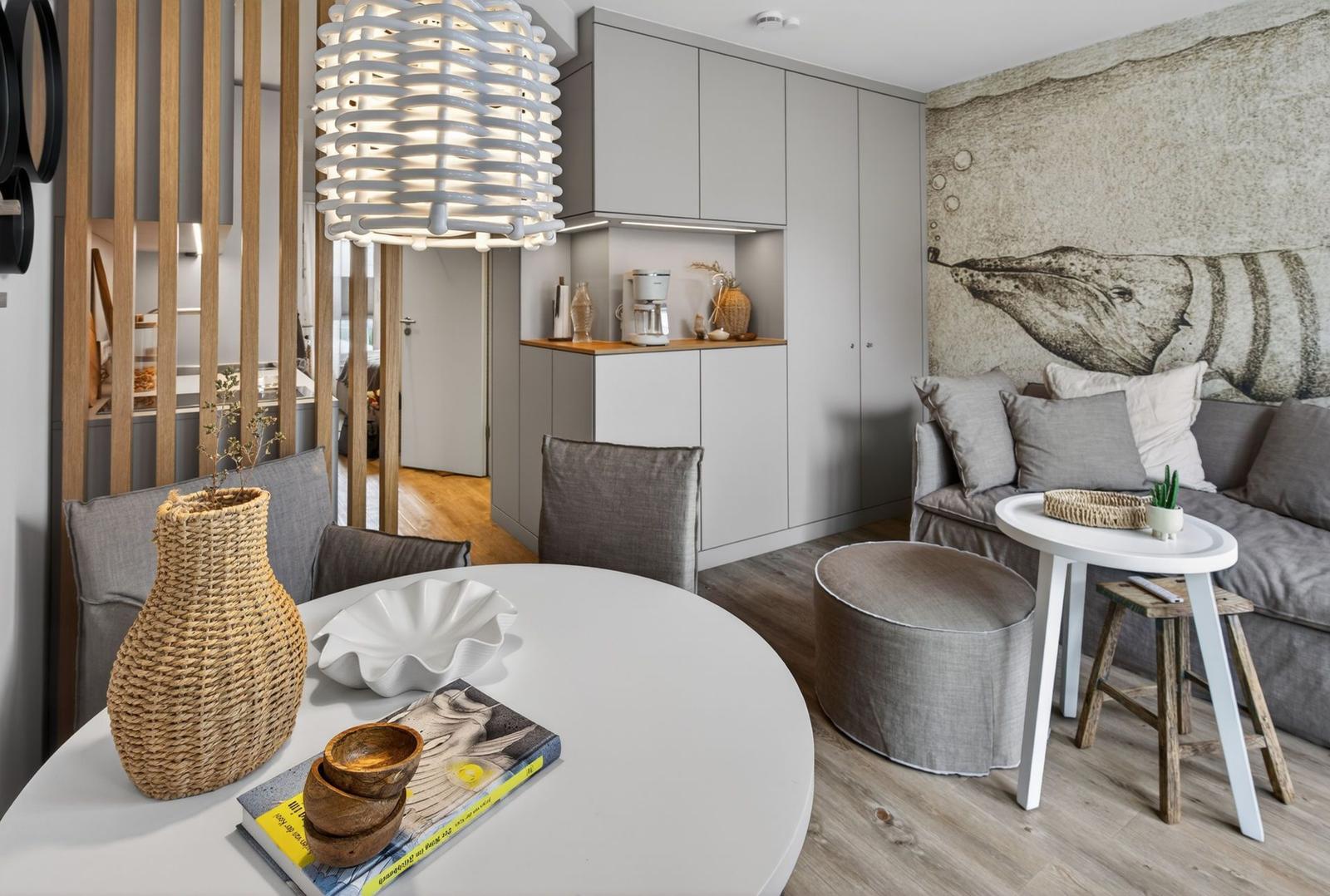 Ein Wohn- und Essbereich mit grauem Sofa, runden Tischen und einer Wanddekoration mit Wal-Design.