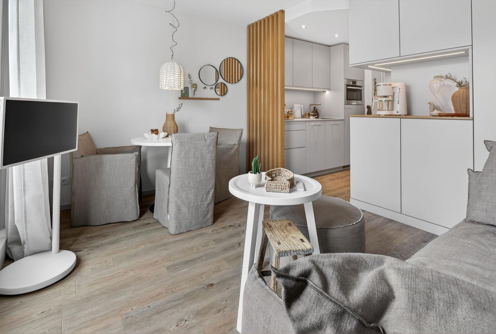 Wohn- und Essbereich mit Küchenbereich. Holzboden, graue Sitzgelegenheiten und weiße Möbel.