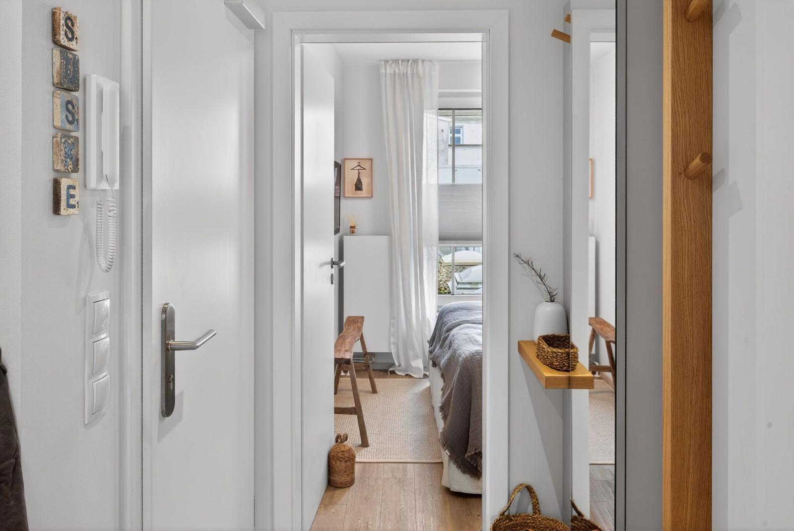 Schlafzimmer mit Bett, Vorhang und Holzstuhl. Türöffnung mit Telefon und Holzregal.