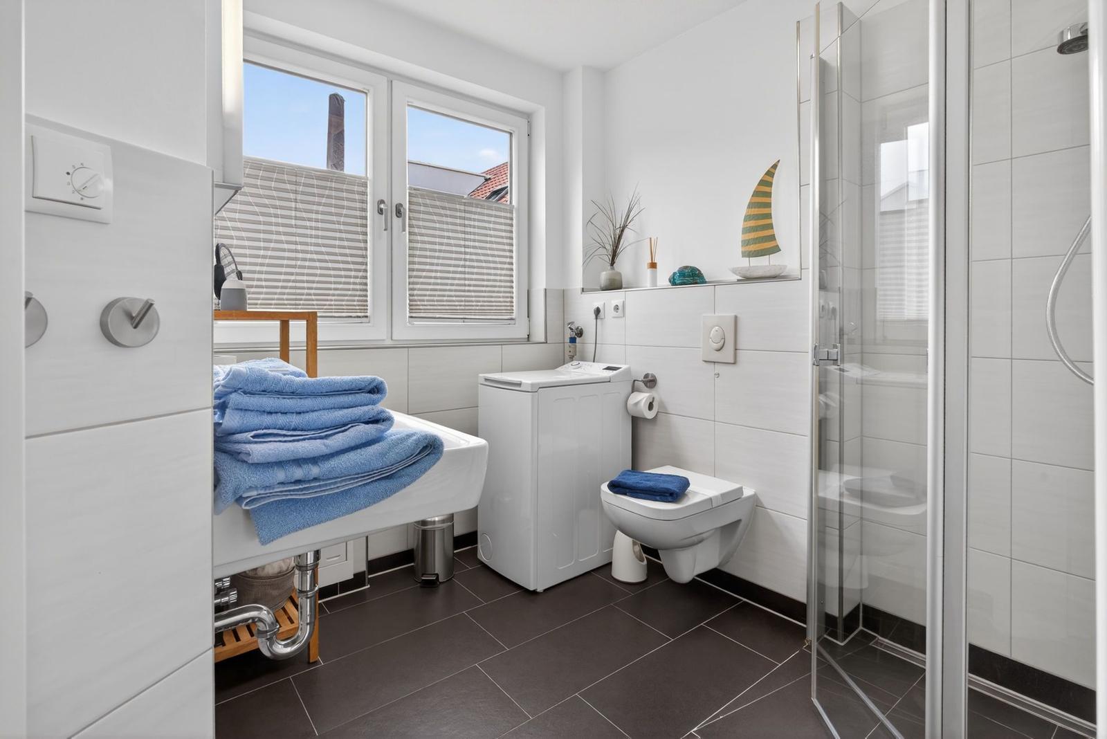 Badezimmer mit Dusche, Toilette, Waschmaschine und Fenster mit Blick.