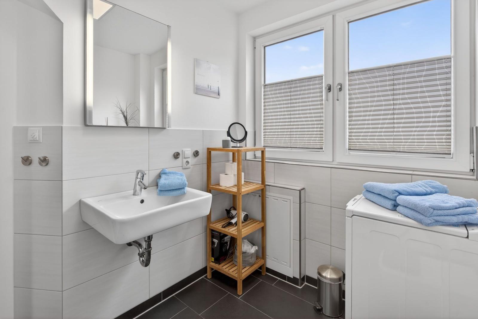 Badezimmer mit Waschbecken, Spiegel, Fenster und Wäschetrockner.