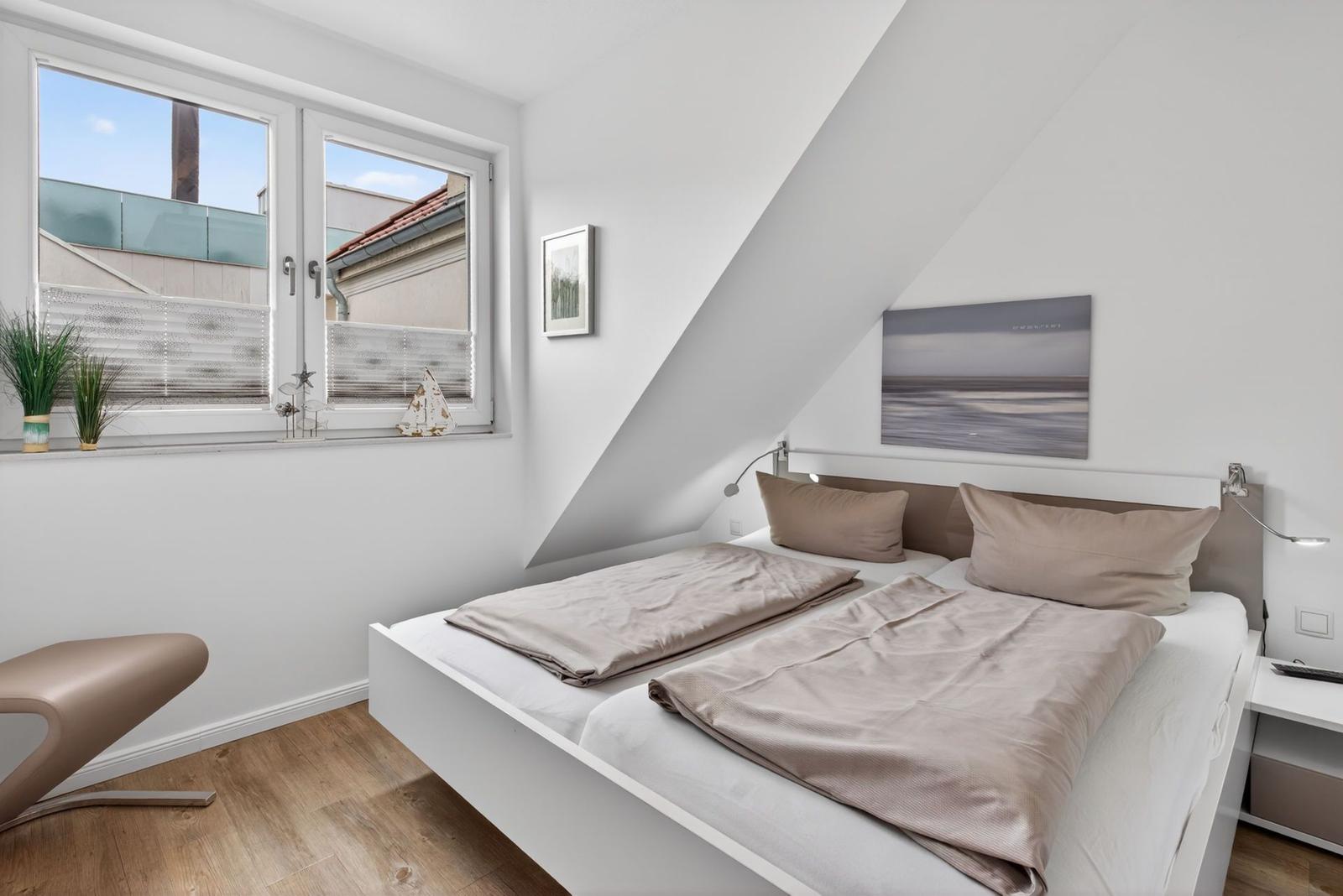 Schlafzimmer mit Dachschrägen, Bett, Fenster und Wandbild.