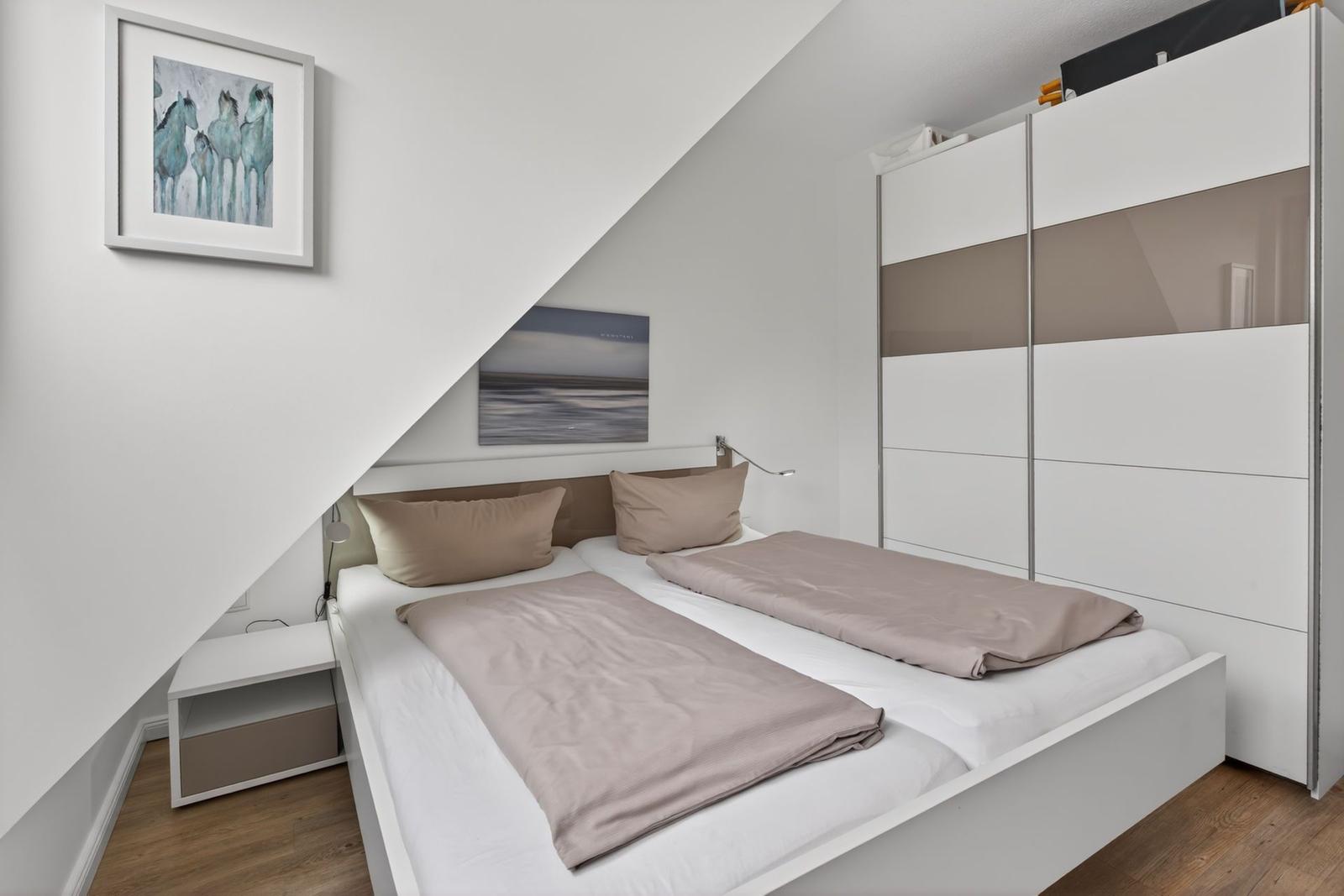 Schlafzimmer mit Doppelbett, Kleiderschrank und Wandbildern.