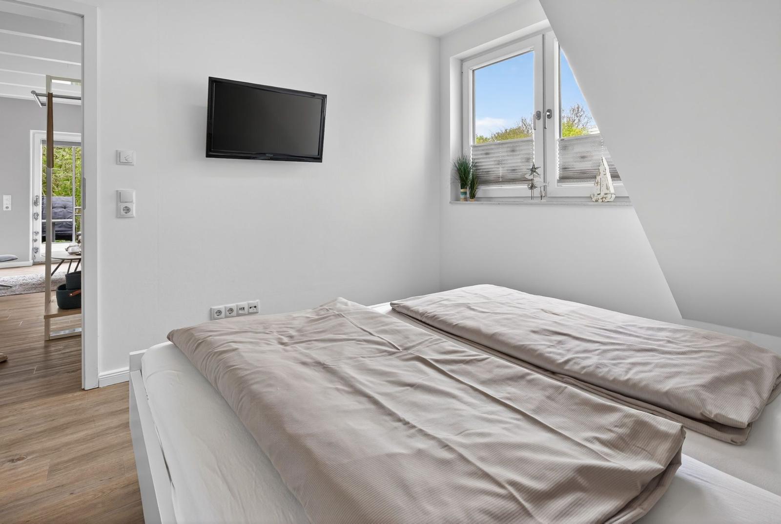 Schlafzimmer mit Doppelbett, Wand-TV und Fenster mit Blick auf Balkon.