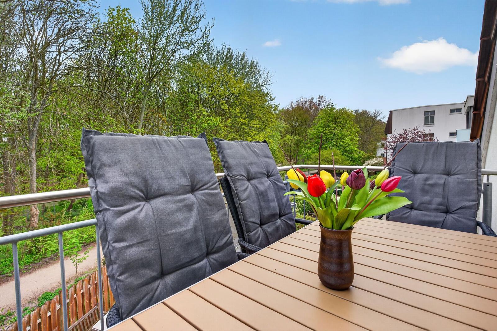 Terrasse mit Tisch, Stühlen und Tulpenblumen. Blick auf Bäume und Gebäude.