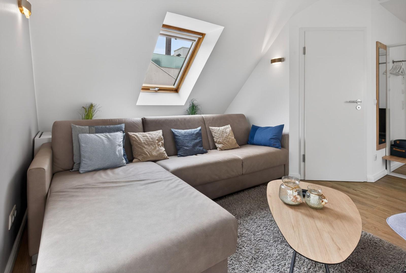 Ein Wohnzimmer mit einem Sofa, einem ovalen Tisch und einem Dachfenster.