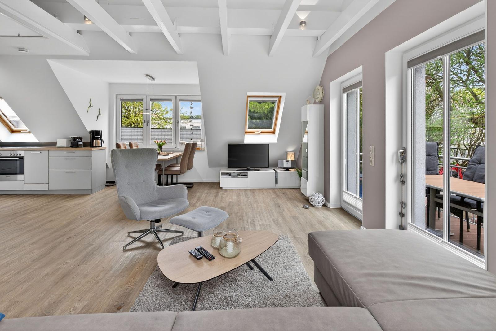 Wohnung mit Essbereich, Küche und Balkon. Holzboden, weiße Deckenbalken und große Fenster.
