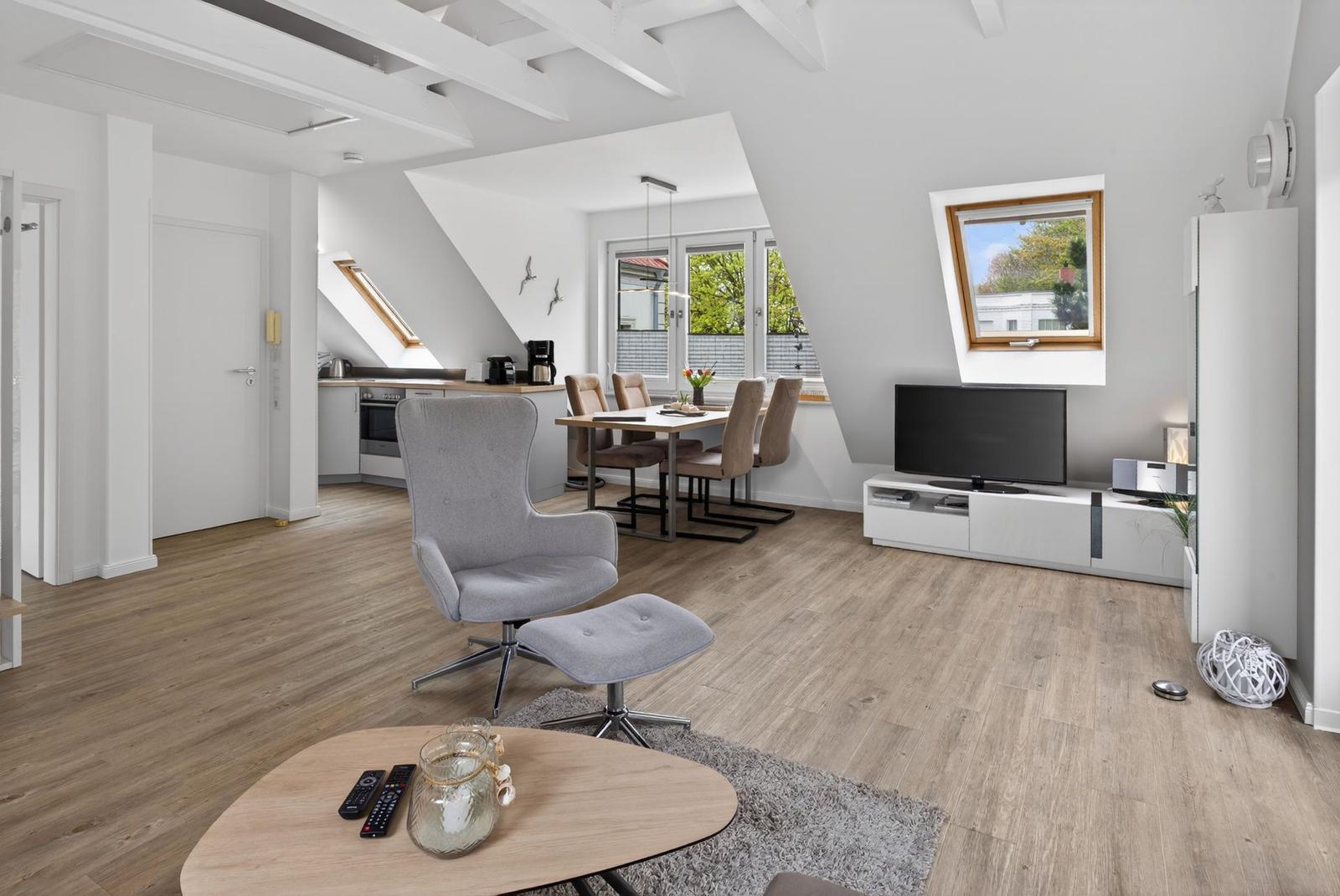 Wohn- und Essbereich mit Küche unter Dachschrägen, TV, Sessel und Holzboden.
