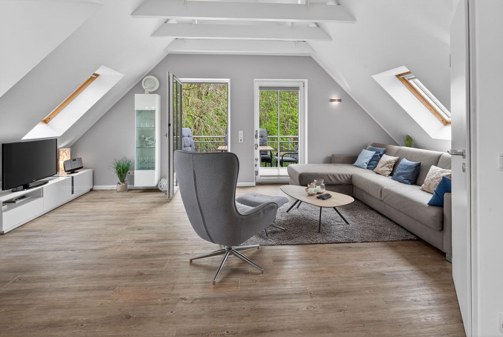 Wohnzimmer mit Sofa, Sessel und TV unter Dachschrägen.