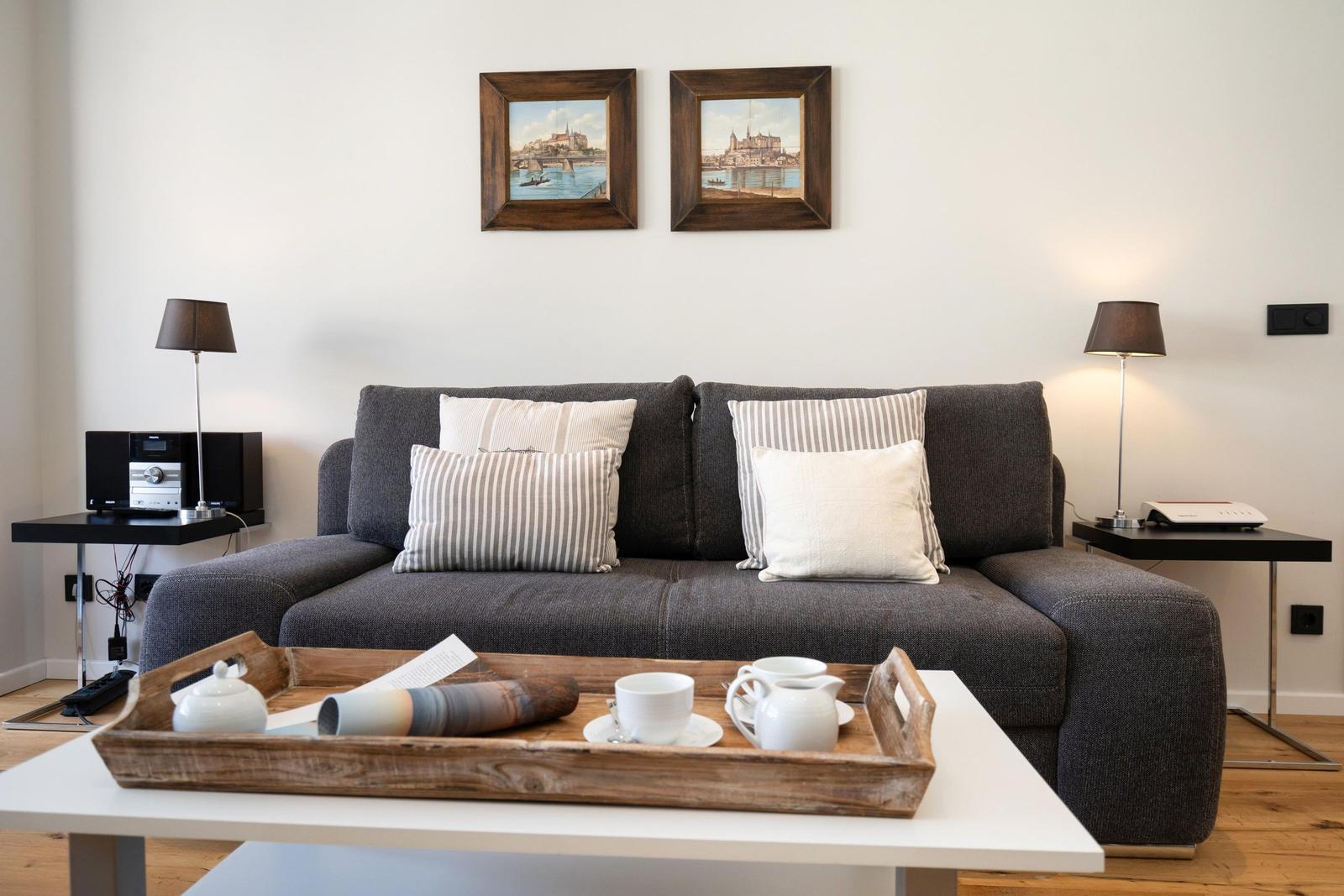 Ein grauer Sofa mit Kissen, Tisch mit Kaffeetablett und Wandbilder.