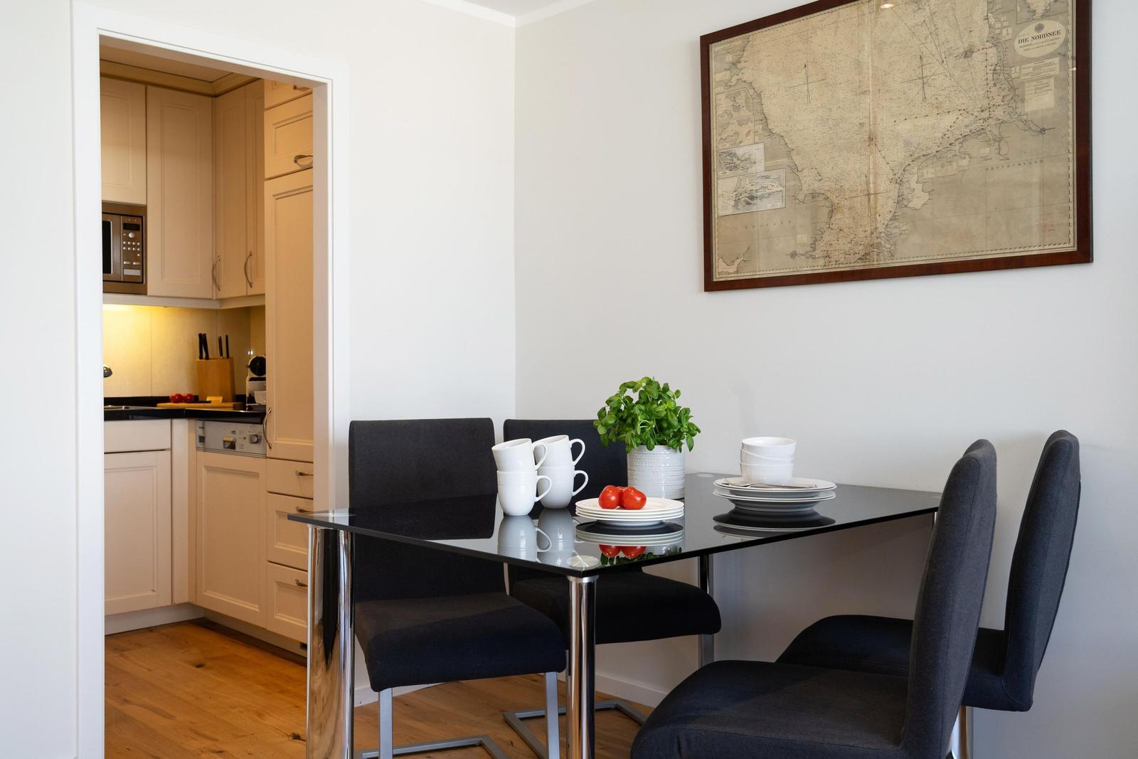 Essbereich mit Tisch, Stühlen und Karte an der Wand. Küche im Hintergrund sichtbar.