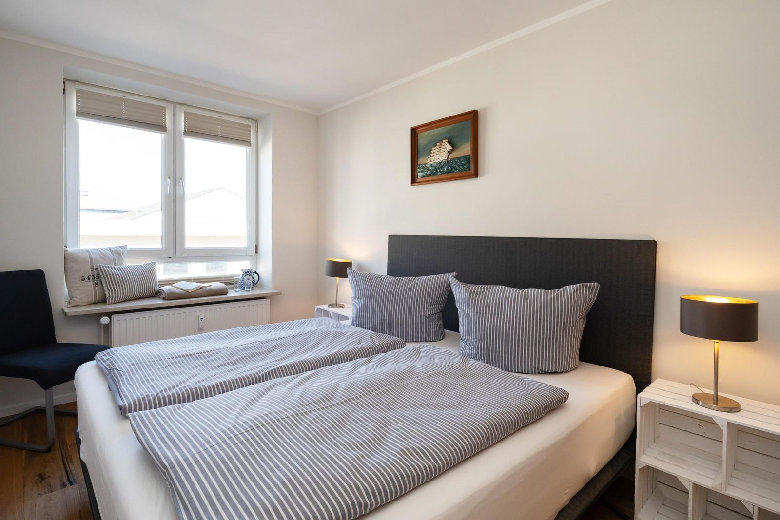 Ein Schlafzimmer mit Bett, Nachttisch und Fenster. An der Wand hängt ein Bild.