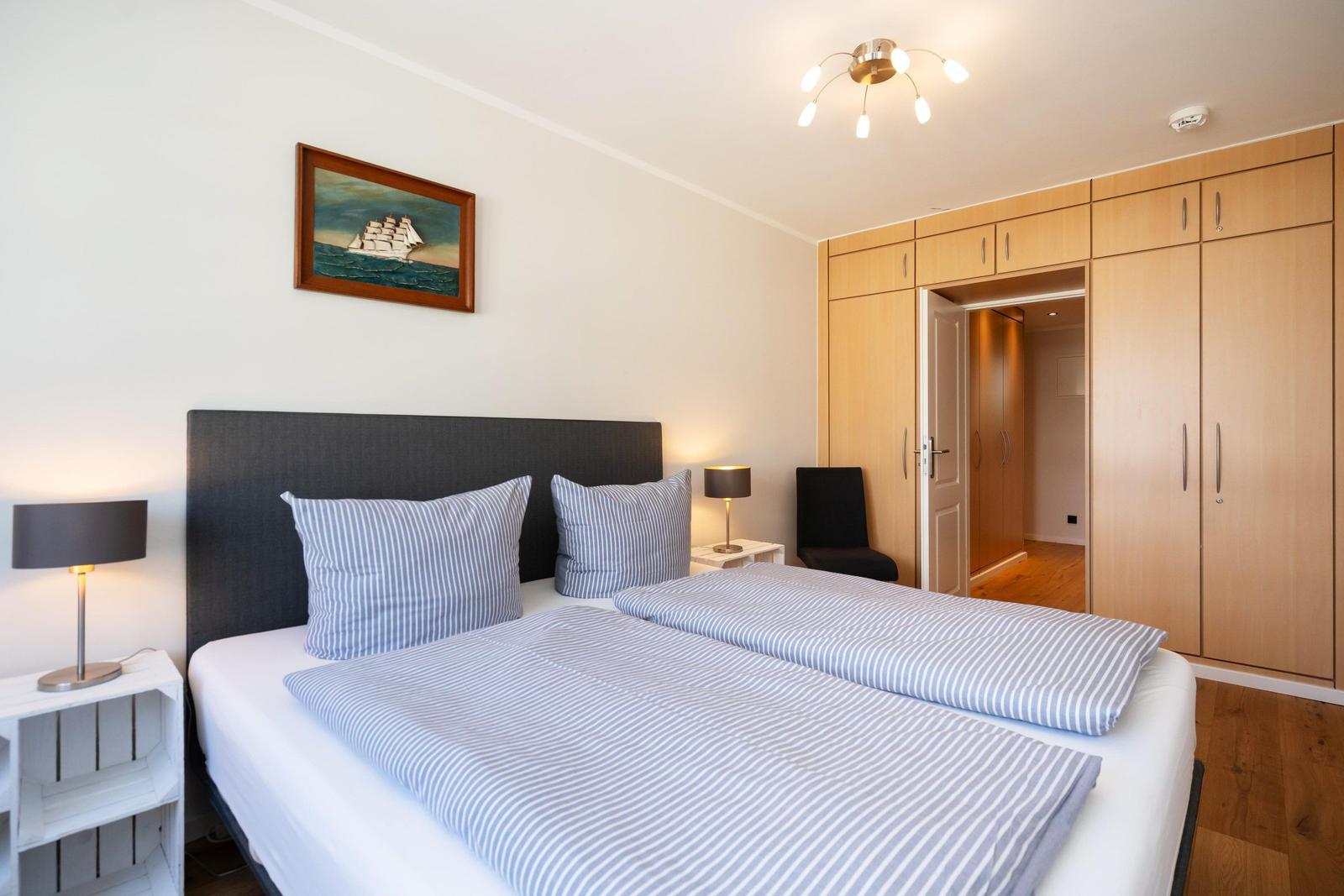 Schlafzimmer mit Doppelbett, Holzschrank und Wandbild eines Segelschiffs.