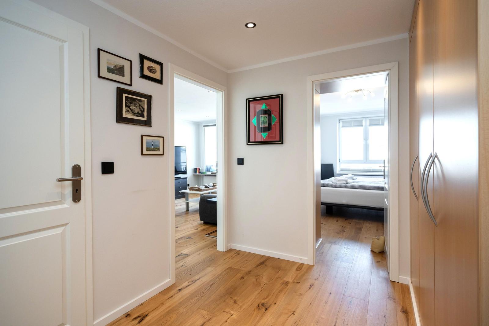 Hausflur mit Holzboden, Wandbildern und Blick in Schlafzimmer und Wohnbereich.