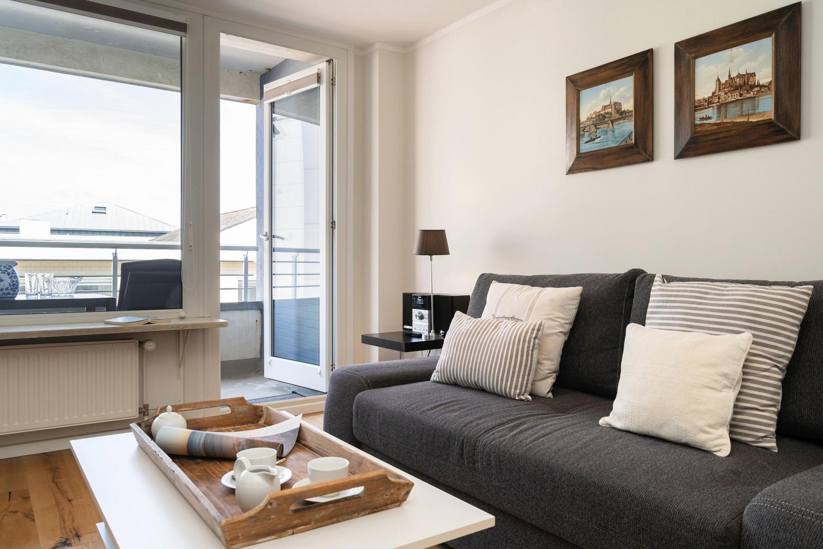 Ein Wohnzimmer mit grauem Sofa, Kissen und einem Tisch mit Teeservice.