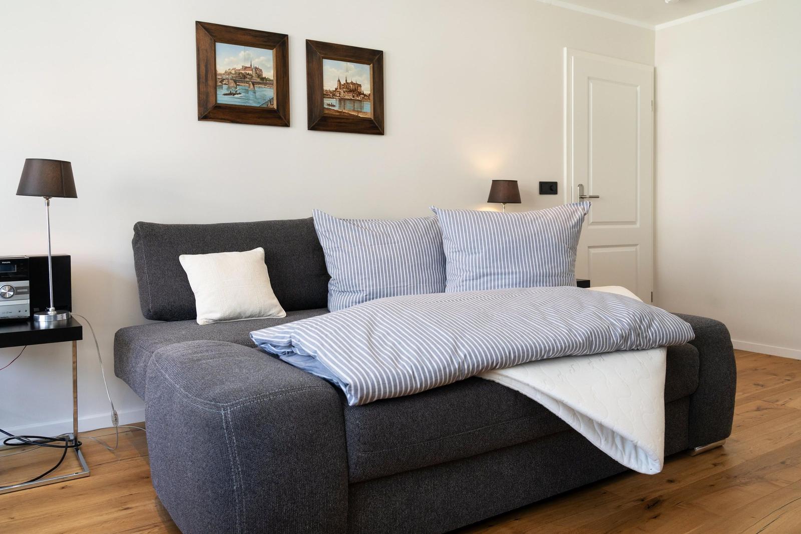 Graße Couch mit Streifen-Bettwäsche und zwei Wandbildern über dem Sofa.