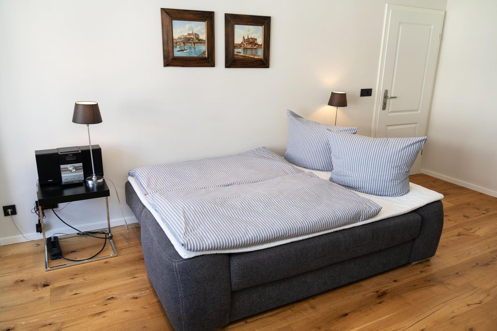 Schlafzimmer mit Bett, Nachttisch, Lampe und Wandbildern.
